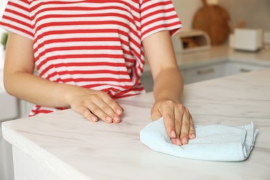 Photo of Woman wiping white marble countertop with rag in kitchen, closeup