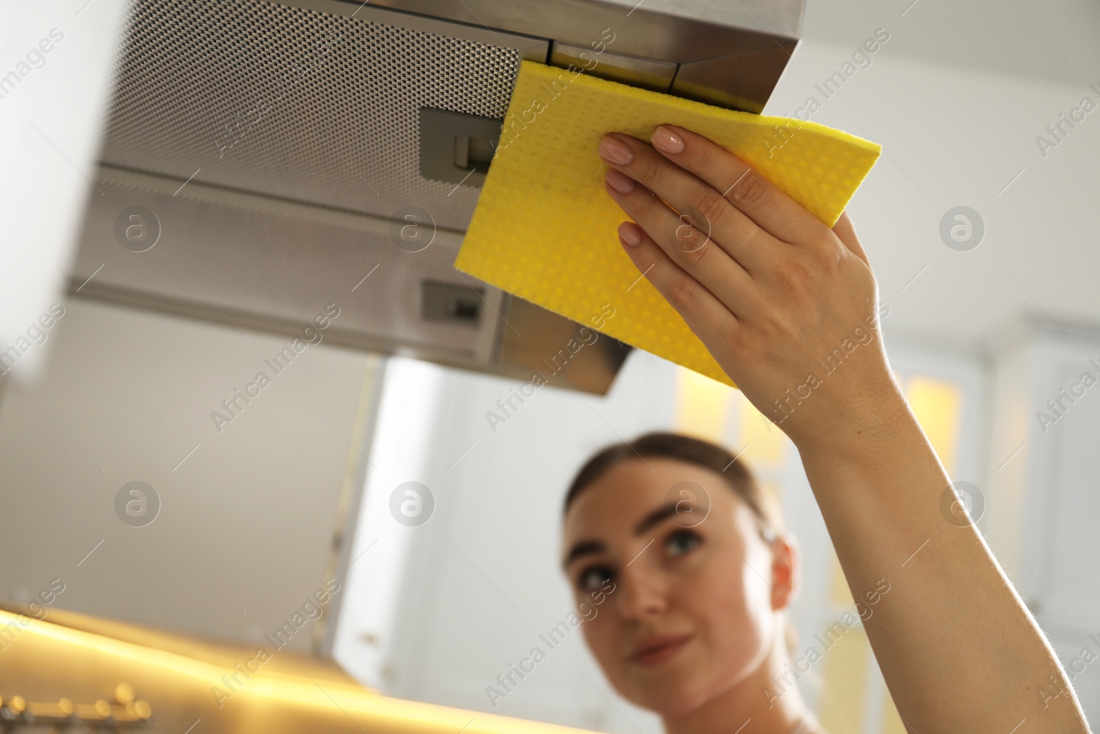 Photo of Beautiful young woman cleaning kitchen hood with napkin at home, selective focus