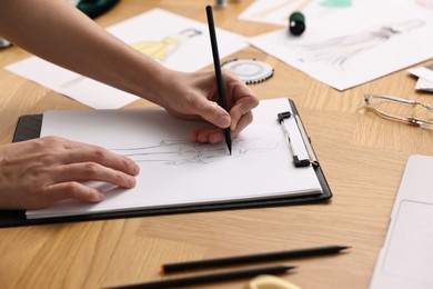 Photo of Fashion designer drawing sketch of beautiful outfit at wooden table, closeup