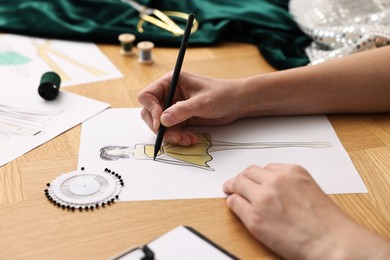 Fashion designer drawing sketch of beautiful dress at wooden table, closeup