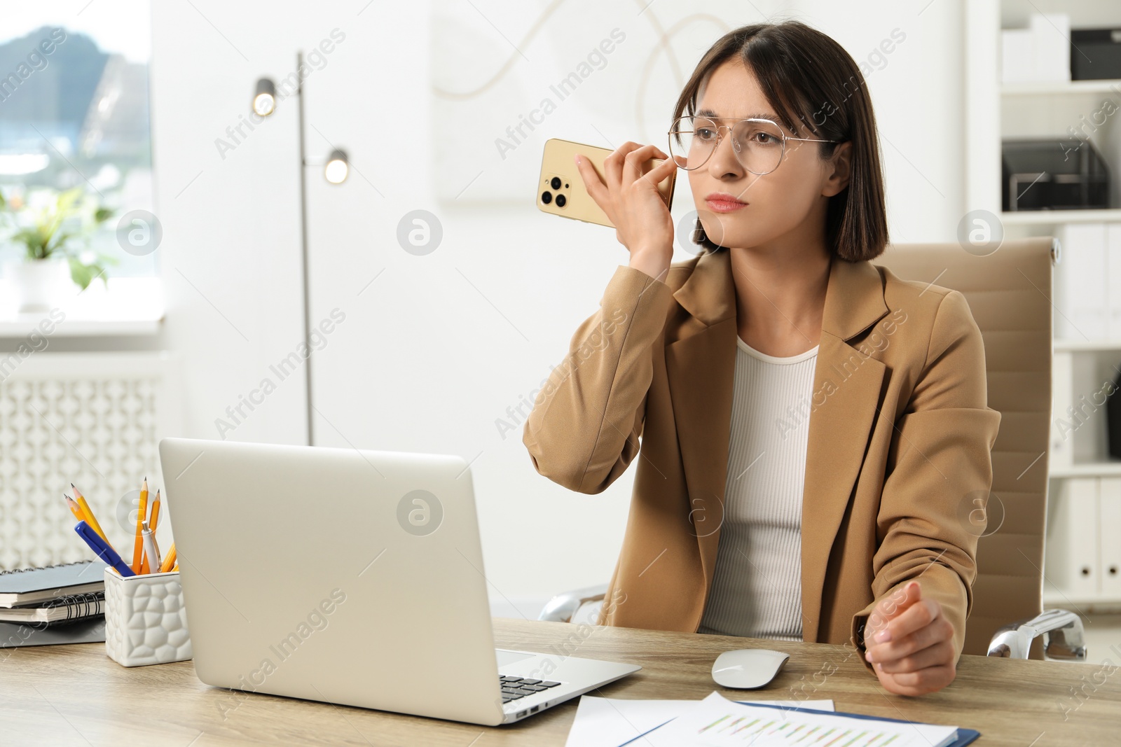 Photo of Beautiful woman with smartphone listening to voice message in office