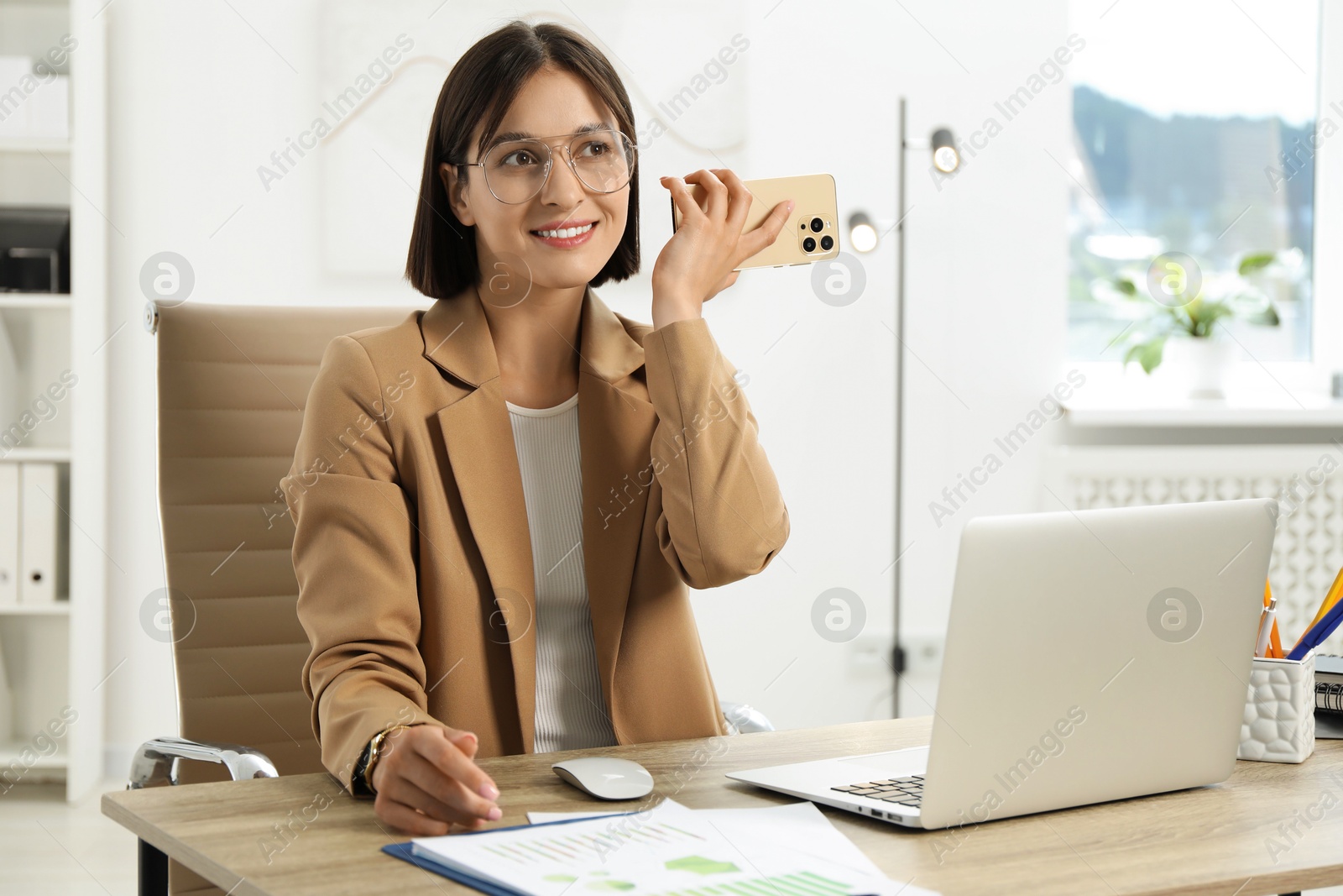 Photo of Beautiful woman with smartphone listening to voice message in office