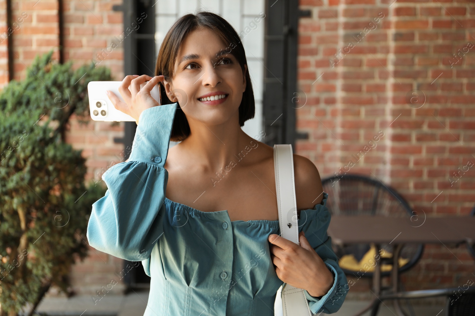 Photo of Beautiful woman with smartphone listening to voice message outdoors