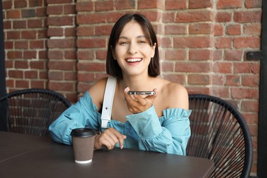 Photo of Beautiful woman recording voice message via smartphone in outdoors cafe