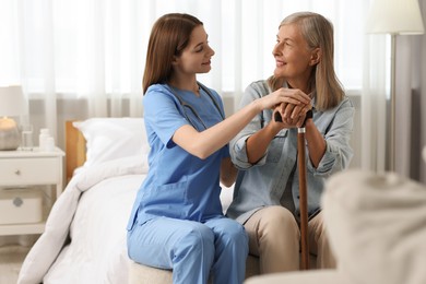 Smiling healthcare worker supporting senior patient on bed indoors