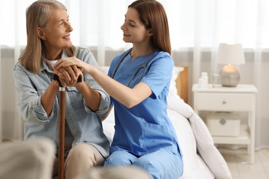 Photo of Smiling healthcare worker supporting senior patient on bed indoors. Space for text