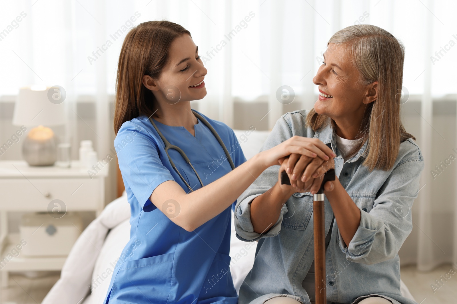 Photo of Smiling healthcare worker supporting senior patient on bed indoors