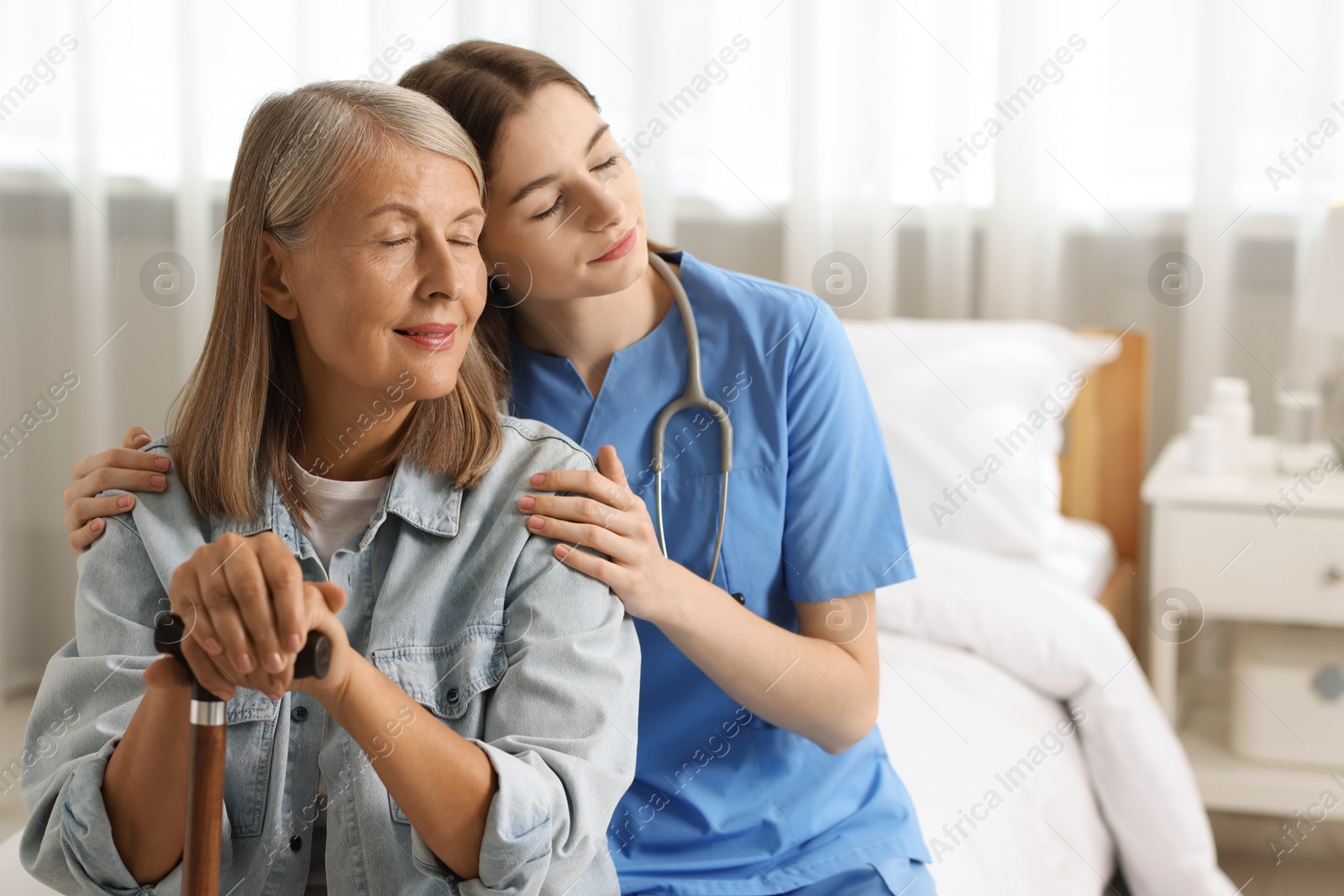 Photo of Young healthcare worker supporting senior patient on bed indoors. Space for text