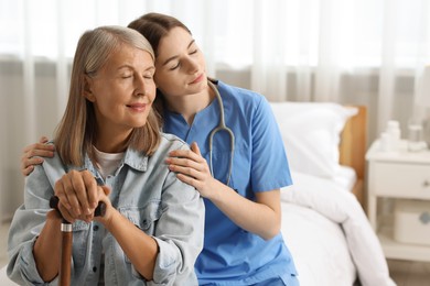 Photo of Young healthcare worker supporting senior patient on bed indoors. Space for text