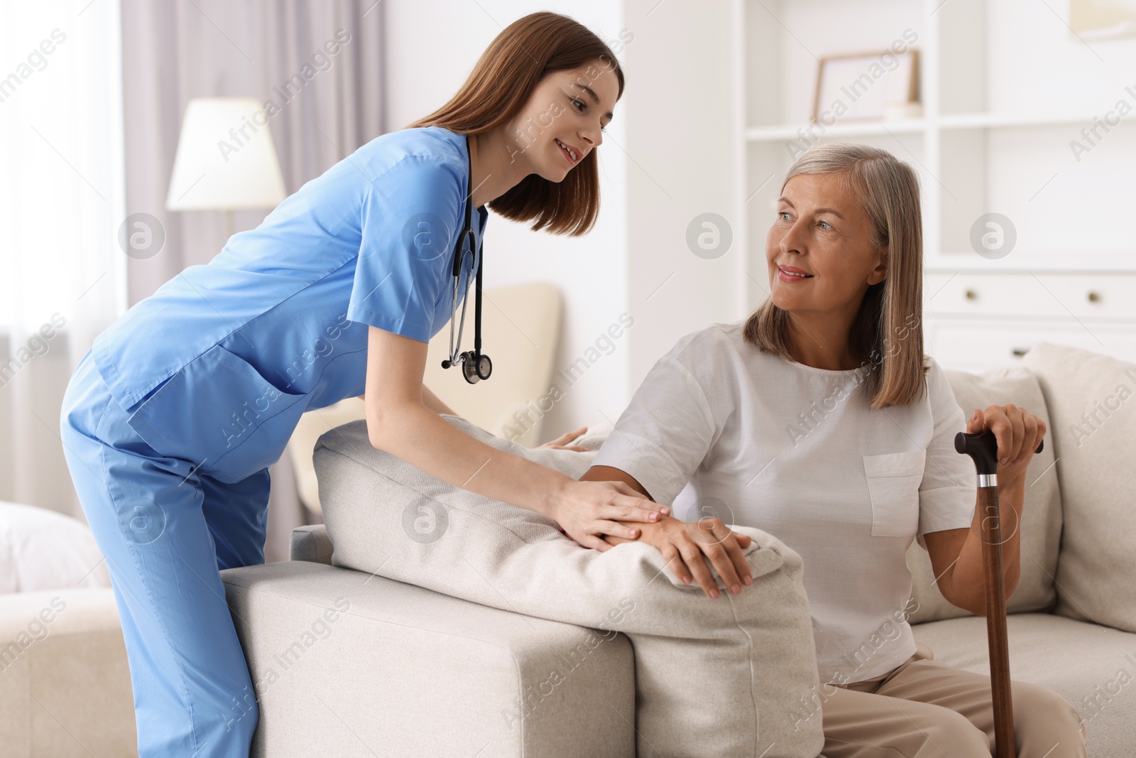 Photo of Smiling healthcare worker supporting senior patient indoors