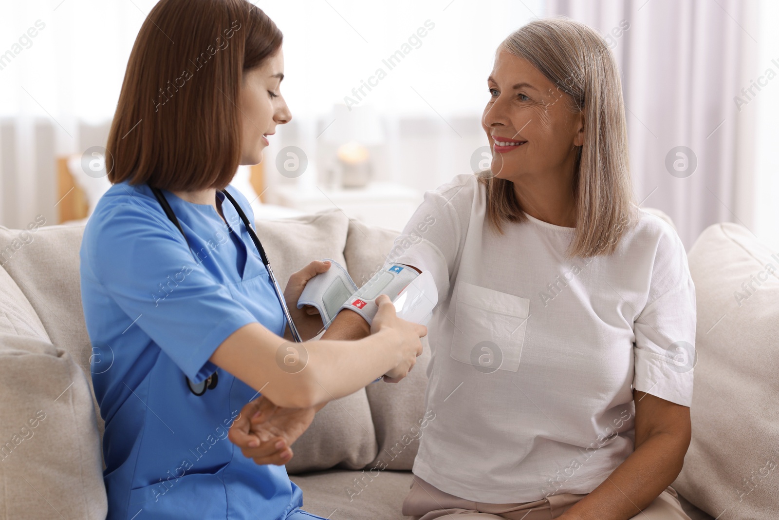 Photo of Young healthcare worker measuring patient's blood pressure indoors