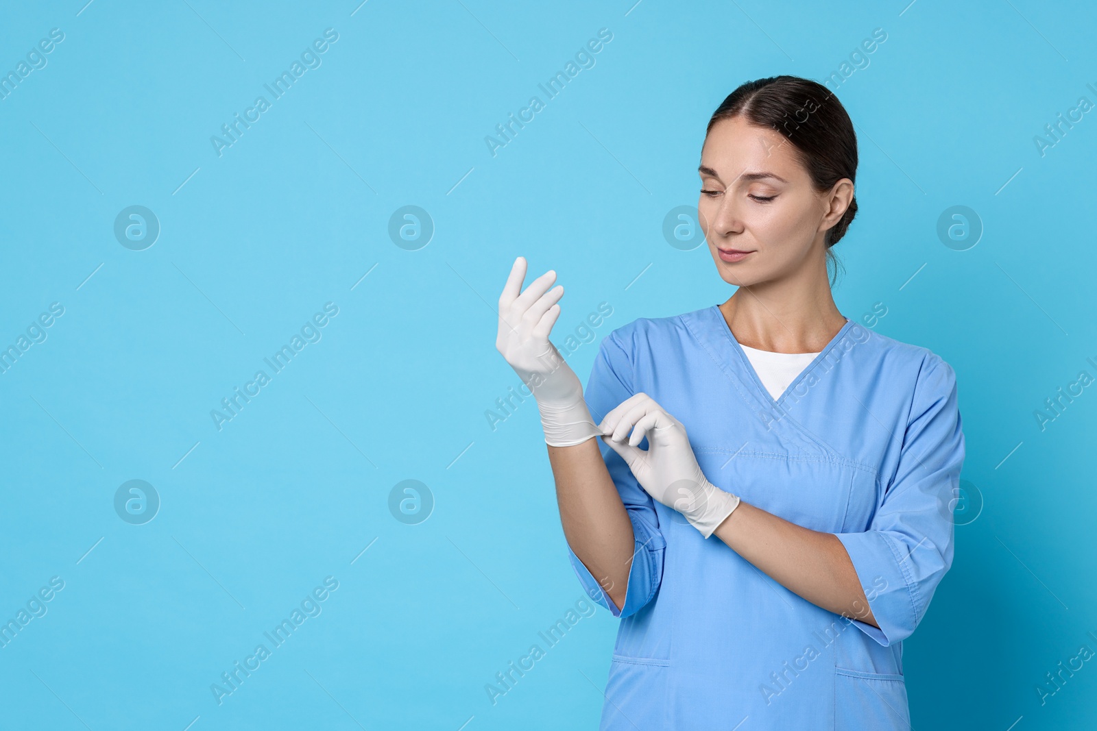 Photo of Nurse in medical uniform wearing gloves on light blue background, space for text