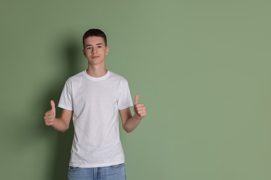 Teenage boy wearing white t-shirt and showing thumbs up on green background, space for text