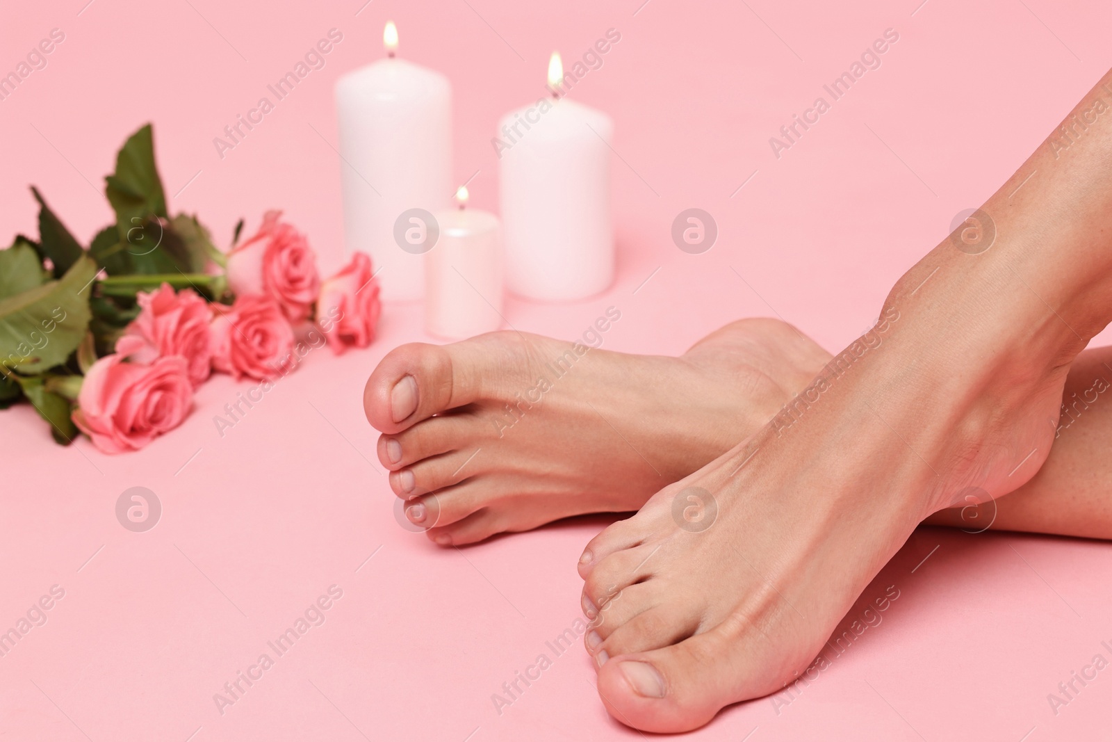 Photo of Woman with smooth feet, burning candles and roses on pink background, closeup