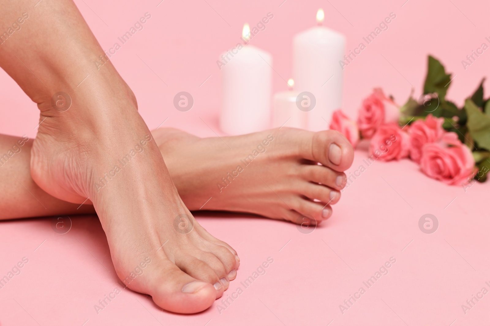 Photo of Woman with smooth feet, burning candles and roses on pink background, closeup