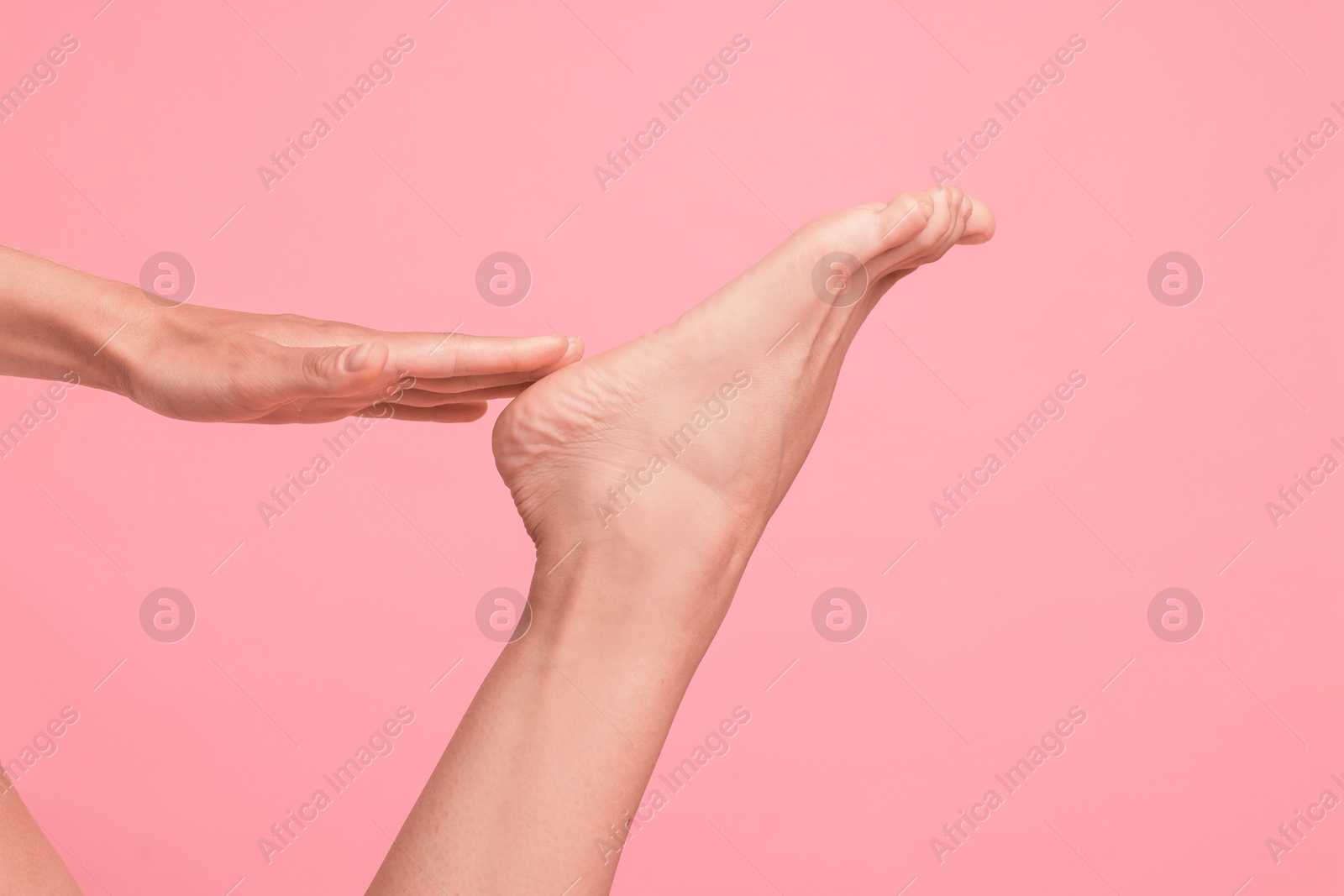 Woman touching her smooth feet on pink background, closeup Photo of Woman touching her smooth feet on pink background, closeup