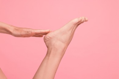 Photo of Woman touching her smooth feet on pink background, closeup