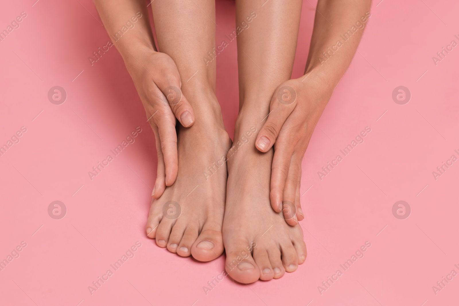 Photo of Woman touching her smooth feet on pink background, closeup