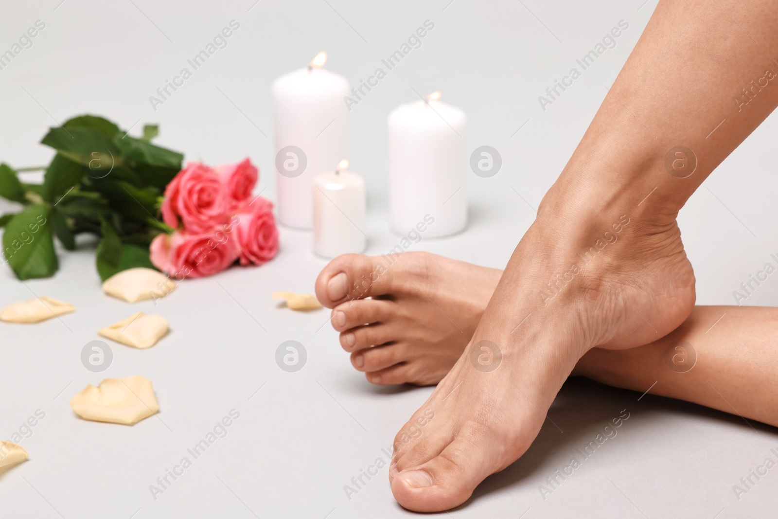 Photo of Woman with smooth feet, burning candles, petals and flowers on grey background, closeup