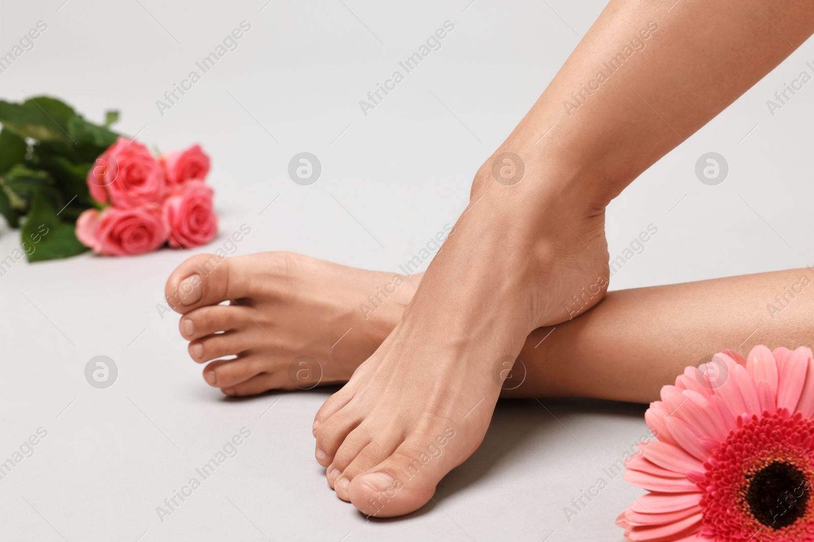 Photo of Woman with smooth feet and flowers on grey background, closeup