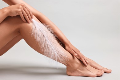 Photo of Woman with smooth legs and feather on grey background, closeup