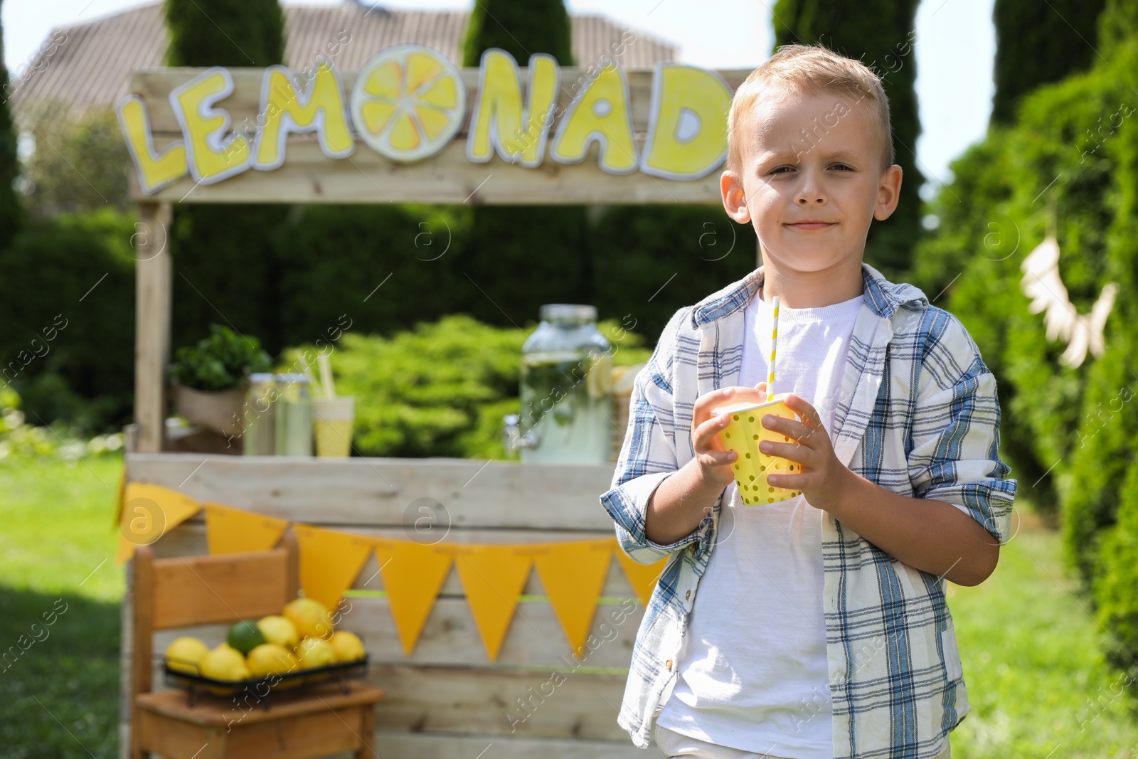 Photo of Cute little boy with refreshing drink near lemonade stand in park