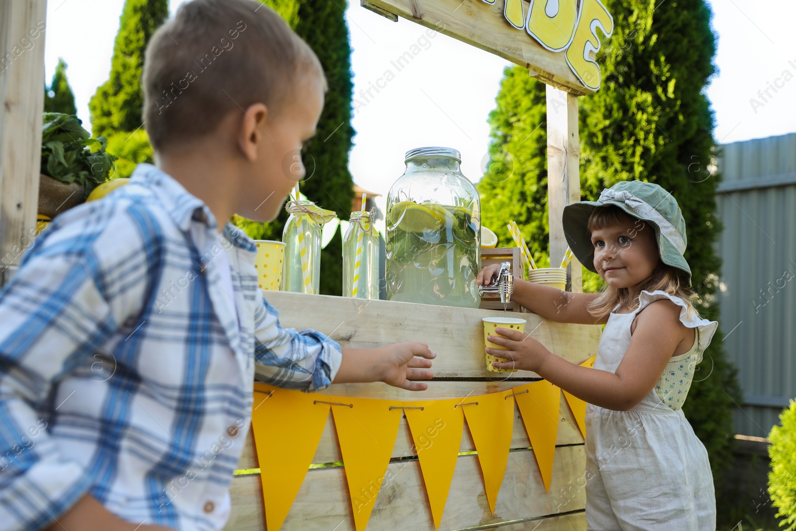 Photo of Cute little girl pouring natural lemonade into cup for boy in park