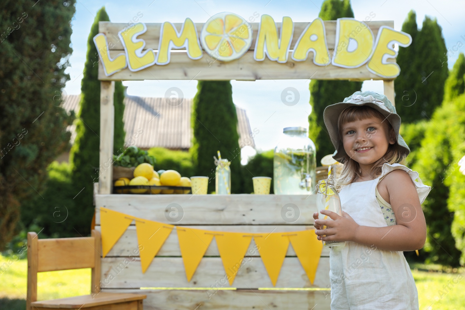 Photo of Cute little girl with refreshing drink near lemonade stand in park