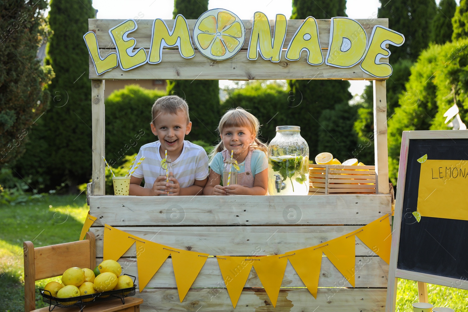 Photo of Cute little kids with refreshing drinks at lemonade stand in park