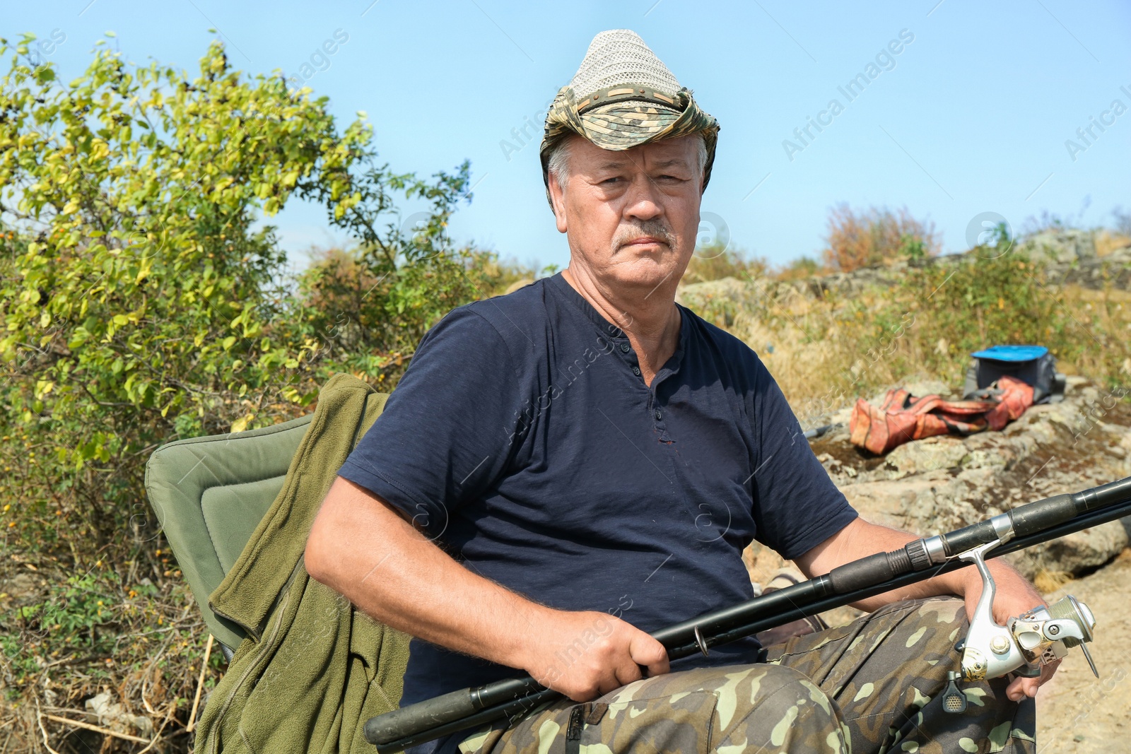 Photo of Fisherman with rod sitting on chair and fishing near lake at summer