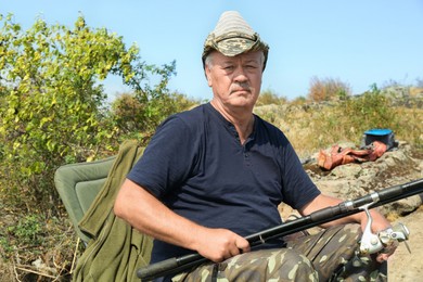 Fisherman with rod sitting on chair and fishing near lake at summer