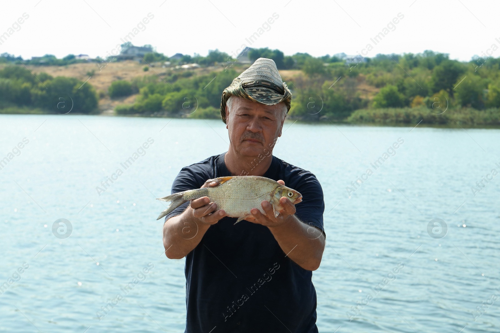 Photo of Fisherman holding caught fish near lake outdoors