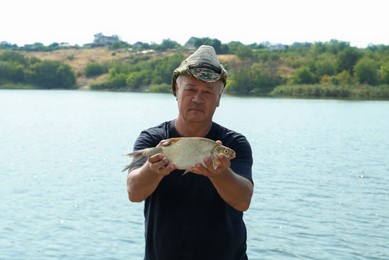 Fisherman holding caught fish near lake outdoors