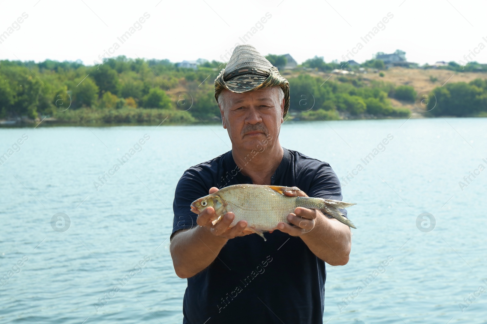 Photo of Fisherman holding caught fish near lake outdoors