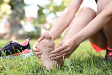 Photo of Woman suffering from foot pain on green grass outdoors, closeup