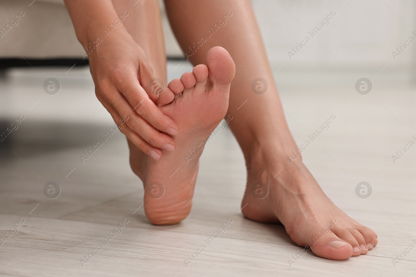 Photo of Woman suffering from foot pain at home, closeup