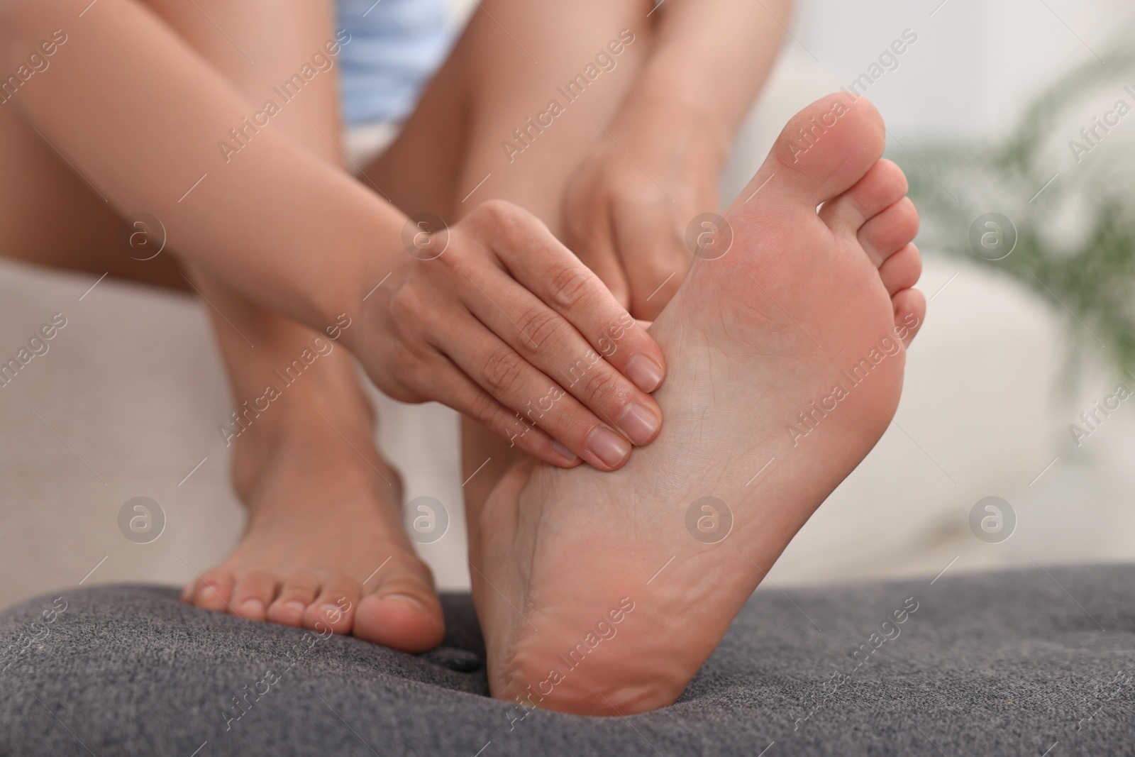 Photo of Woman suffering from foot pain at home, closeup