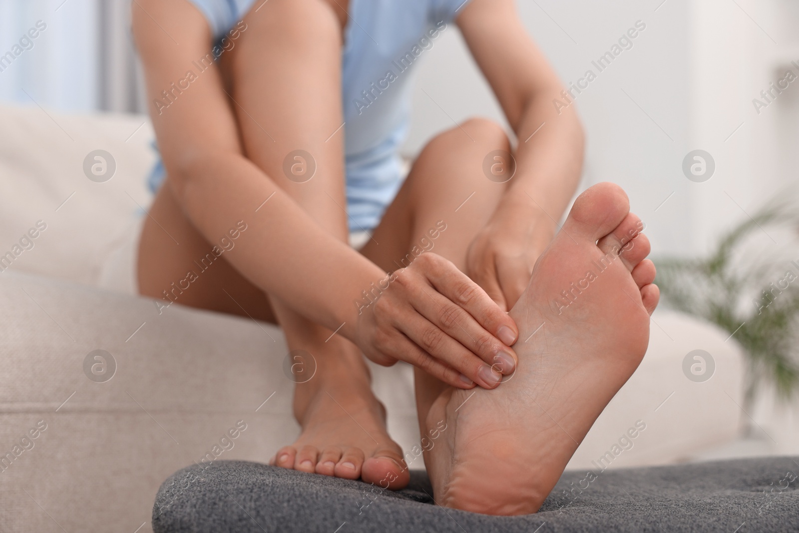 Photo of Woman suffering from foot pain at home, closeup