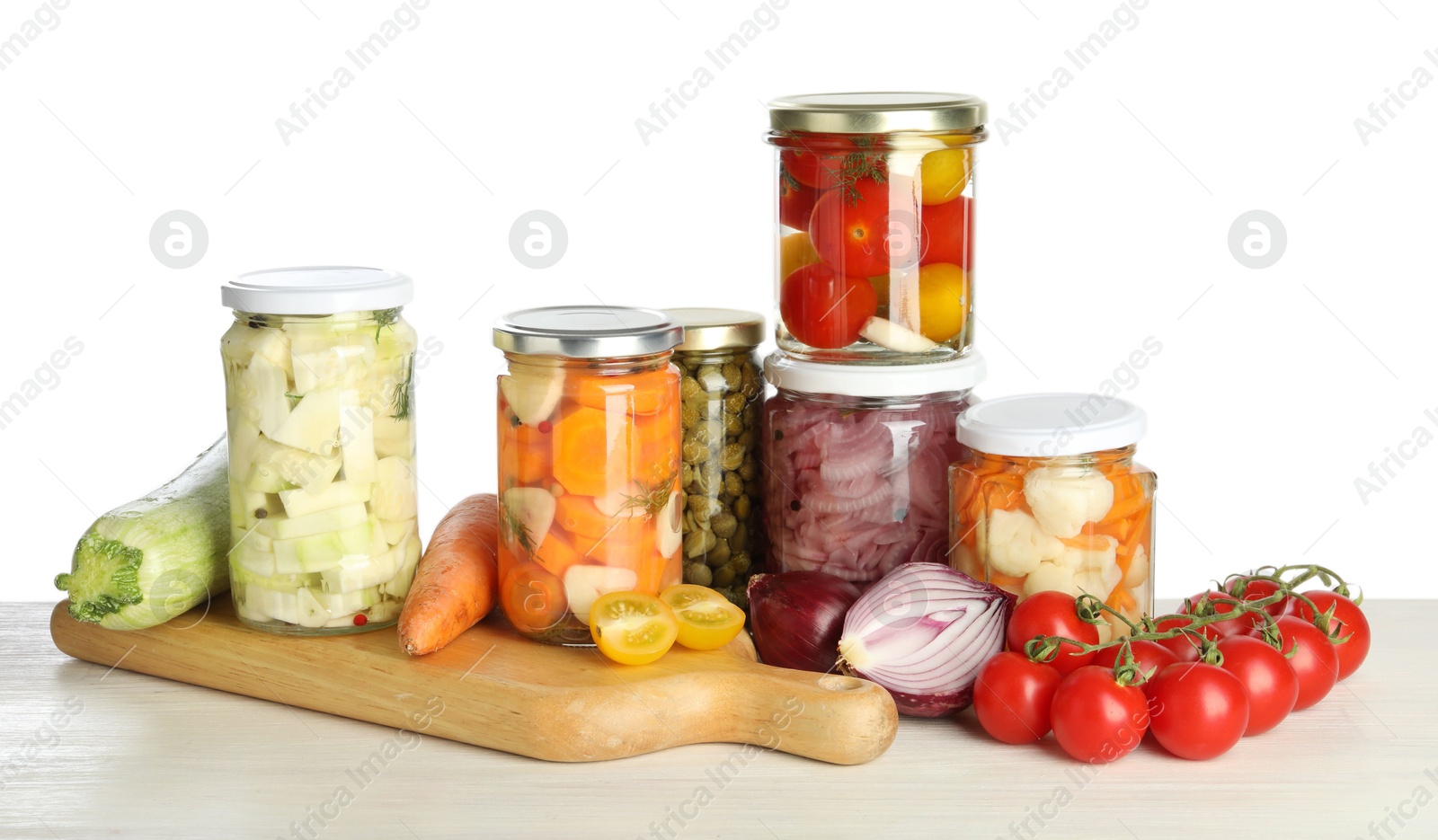 Photo of Different pickled products in jars and fresh vegetables on light wooden table against white background