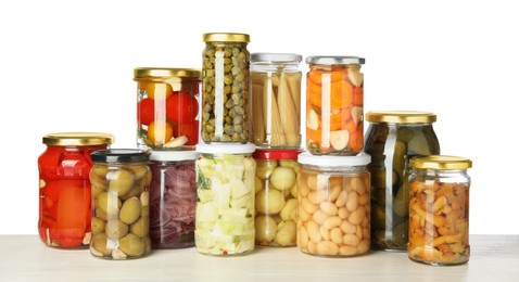 Photo of Different pickled products in jars on light wooden table against white background