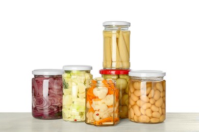 Different pickled products in jars on light wooden table against white background