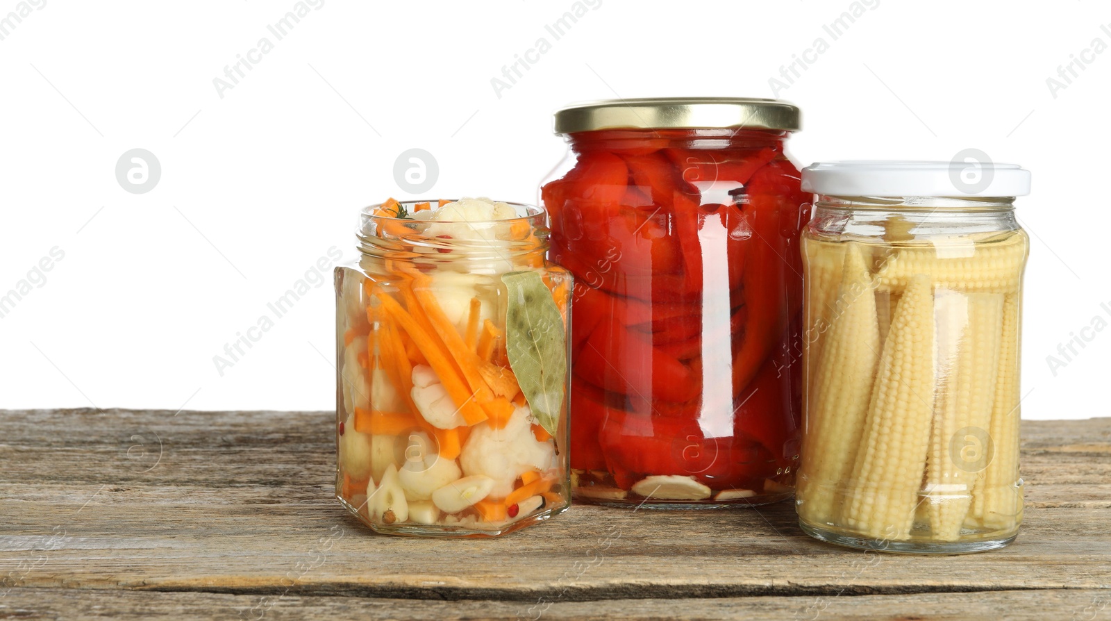 Photo of Different pickled products in jars on wooden table against white background