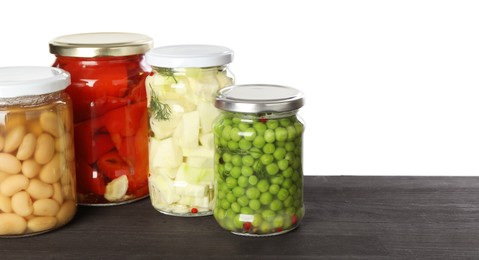 Photo of Different pickled products in jars on dark wooden table against white background. Space for text