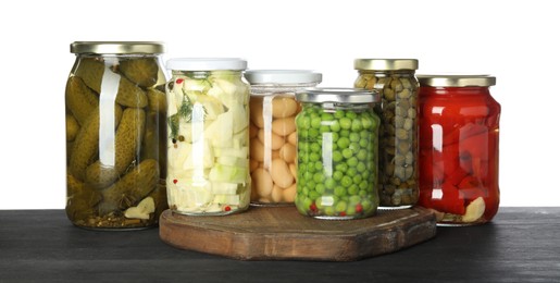 Photo of Different pickled products in jars on dark wooden table against white background