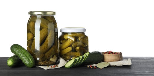 Photo of Tasty pickled cucumbers in jars, fresh vegetables and spices on dark wooden table against white background