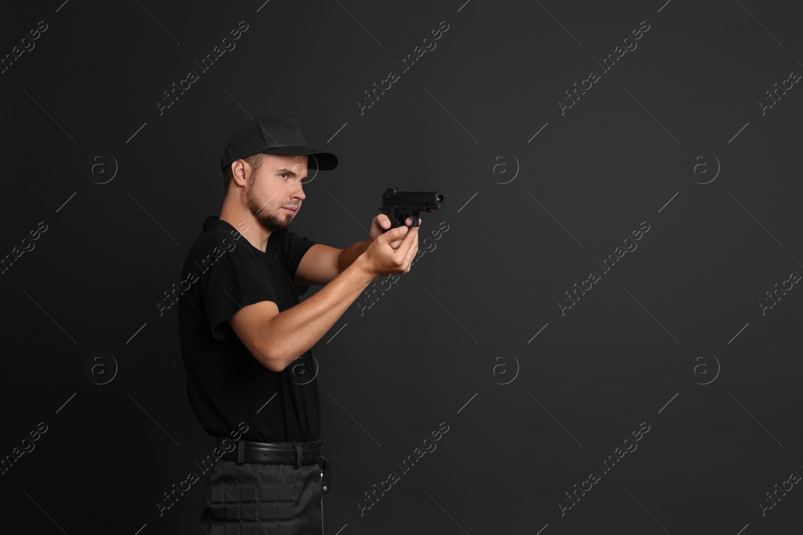 Photo of Young bodyguard using gun on black background, space for text