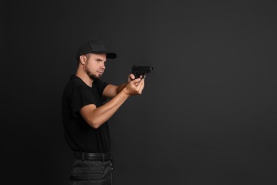 Young bodyguard using gun on black background, space for text