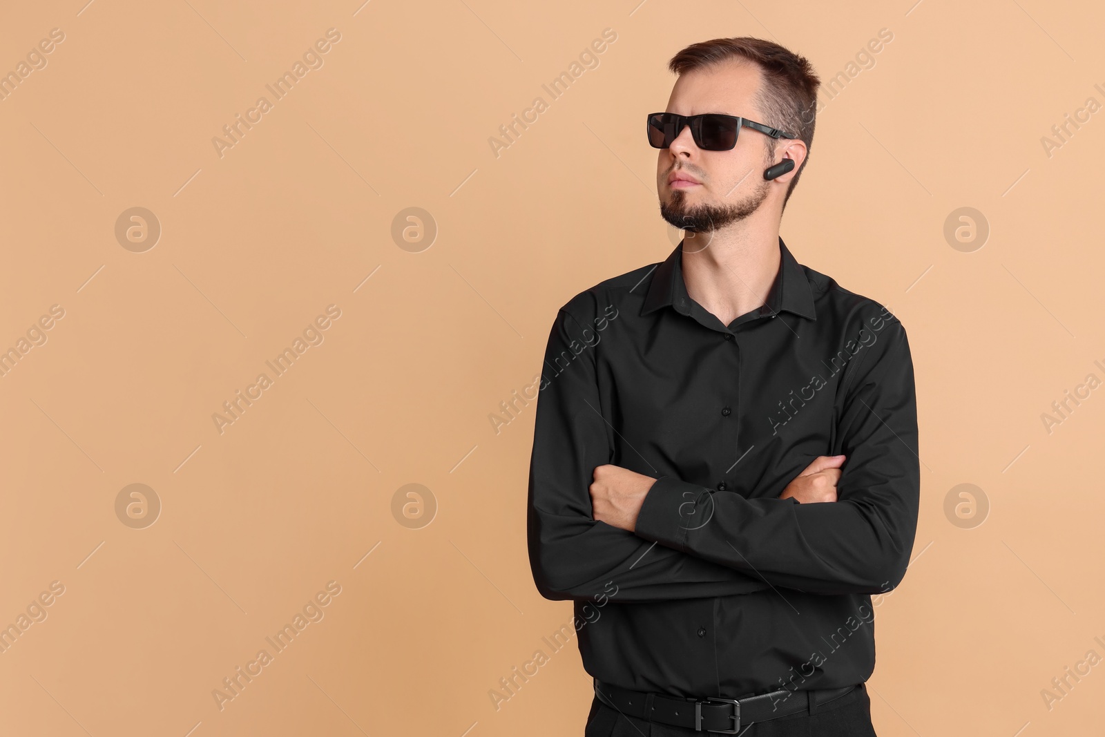 Photo of Young bodyguard in sunglasses and earpiece on beige background, space for text