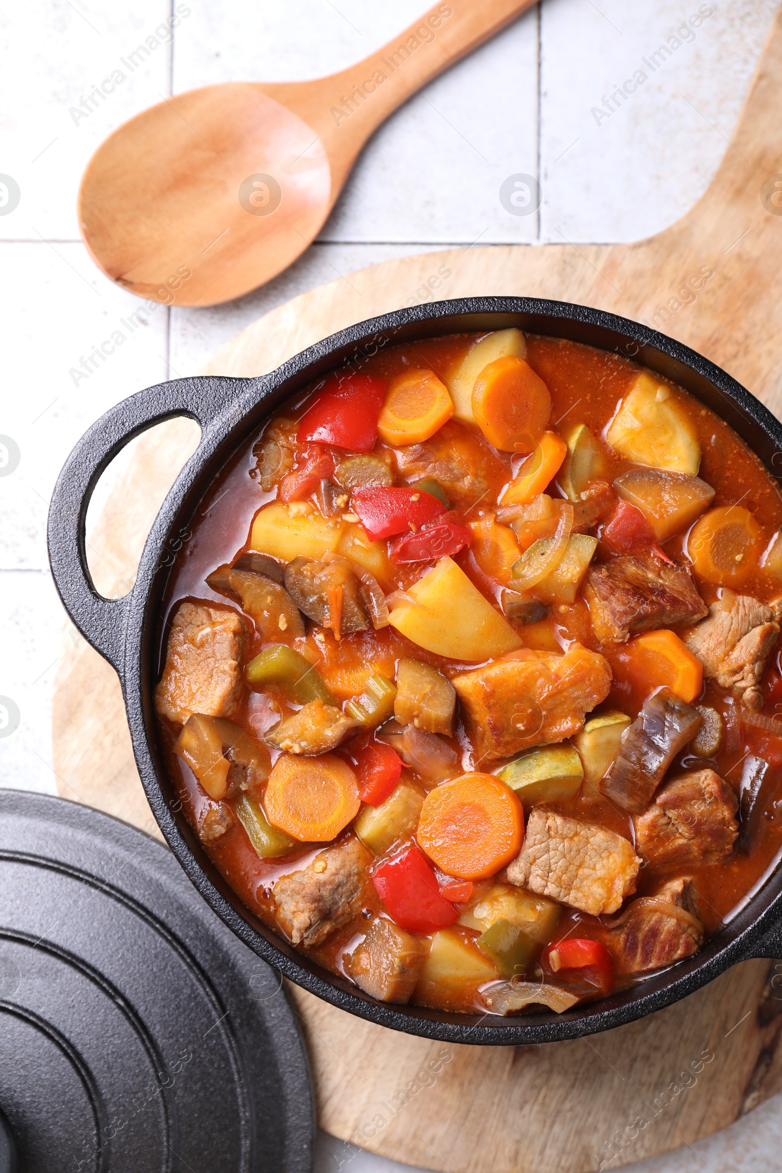 Photo of Delicious stew with vegetables in pot and spoon on light textured table, flat lay