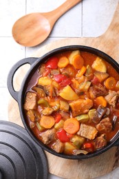 Photo of Delicious stew with vegetables in pot and spoon on light textured table, flat lay